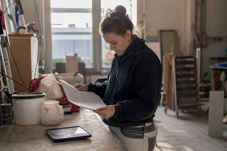 Trockenbauerin arbeitet mit Sicherheitsdatenblättern und Produktgebinden an einem Werkstatttisch